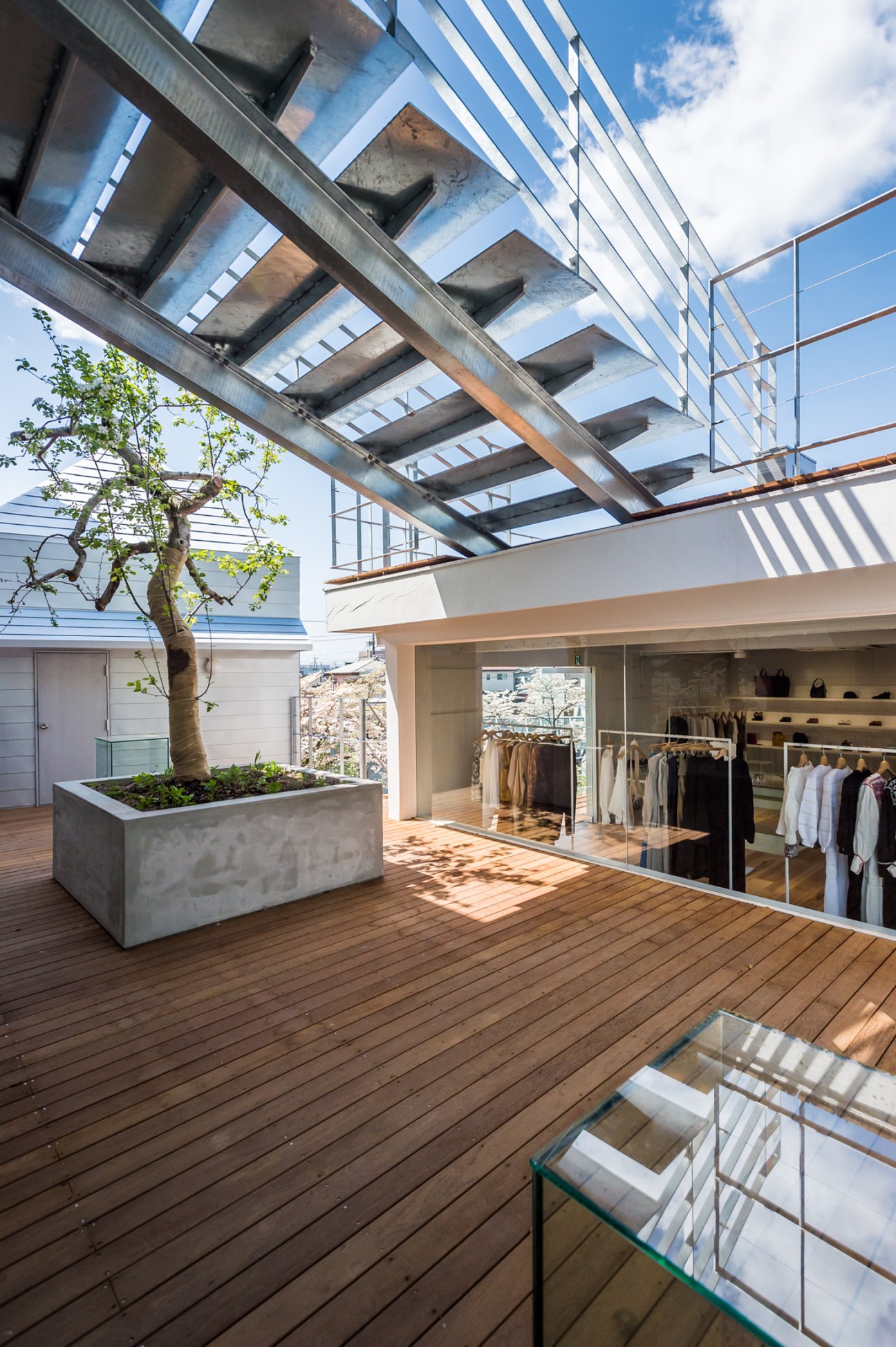 ST Company fashion shop terrace with wooden deck, concrete planter, clothing racks visible through glass doors, and overhead skylight structure.