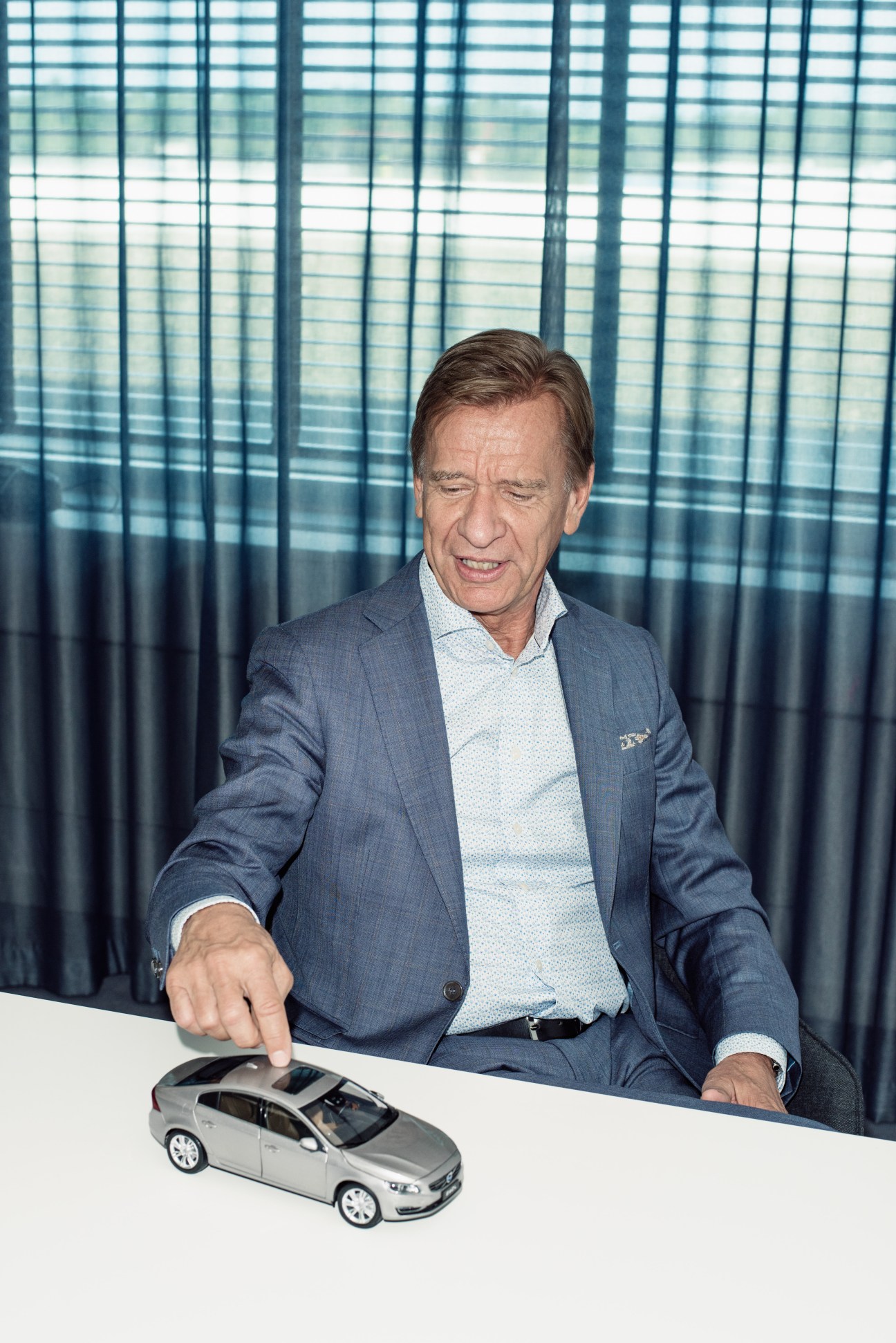 CEO Håkan Samuelsson in a gray suit jacket pointing at a silver Volvo car model on a white table