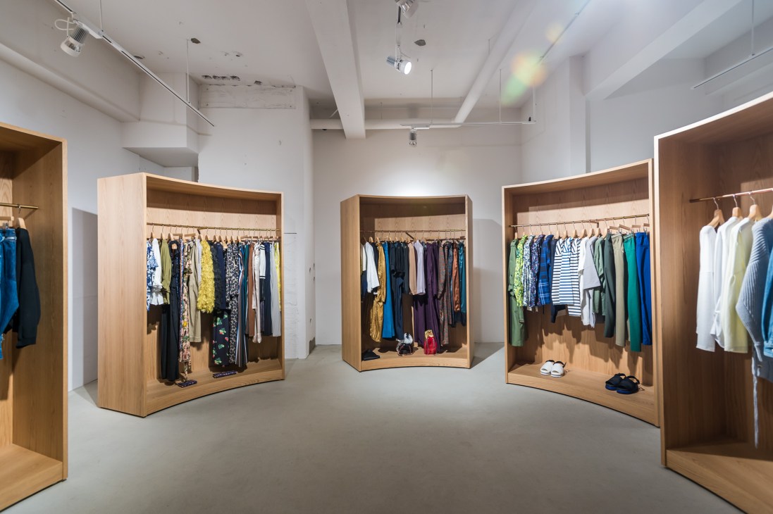 Interior of ST Company fashion shop with wooden display boxes containing clothing on hangers and shoes.