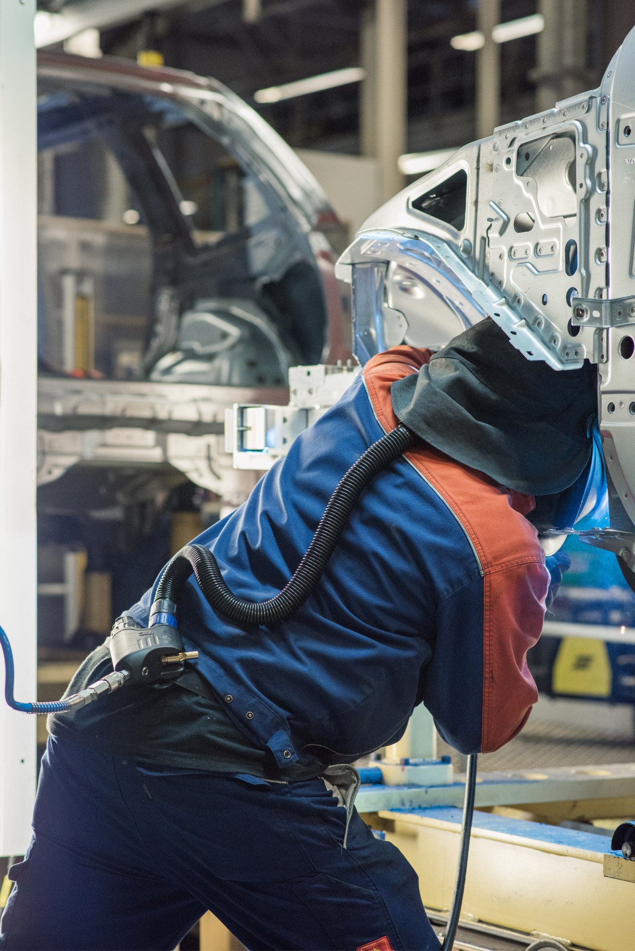 Worker in protective gear welding on Volvo car body in factory production line