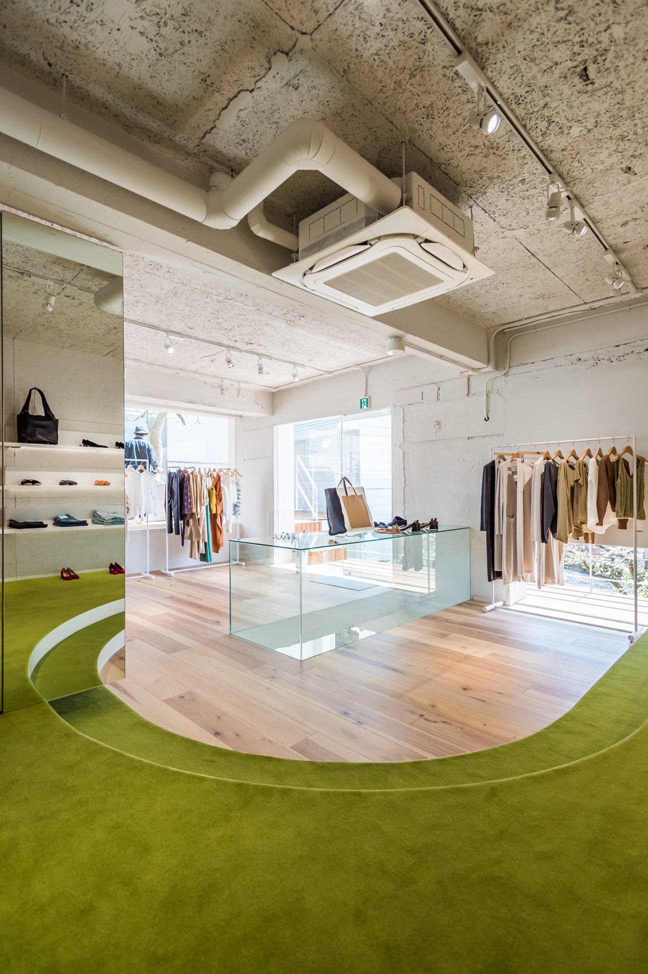 ST Company fashion store interior with natural light, green flooring, wooden display table, clothing racks, and exposed concrete ceiling.