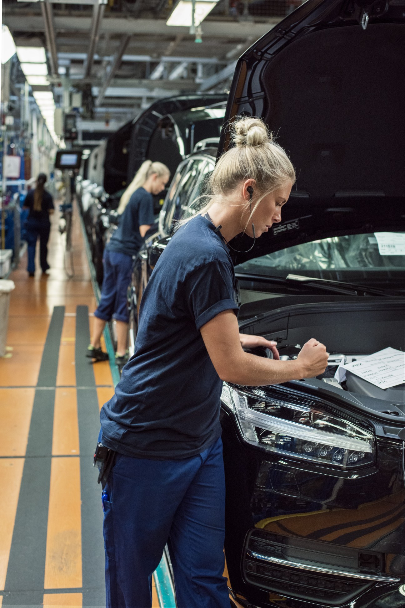Female factory worker in blue uniform inspecting a black car on the Volvo assembly line
