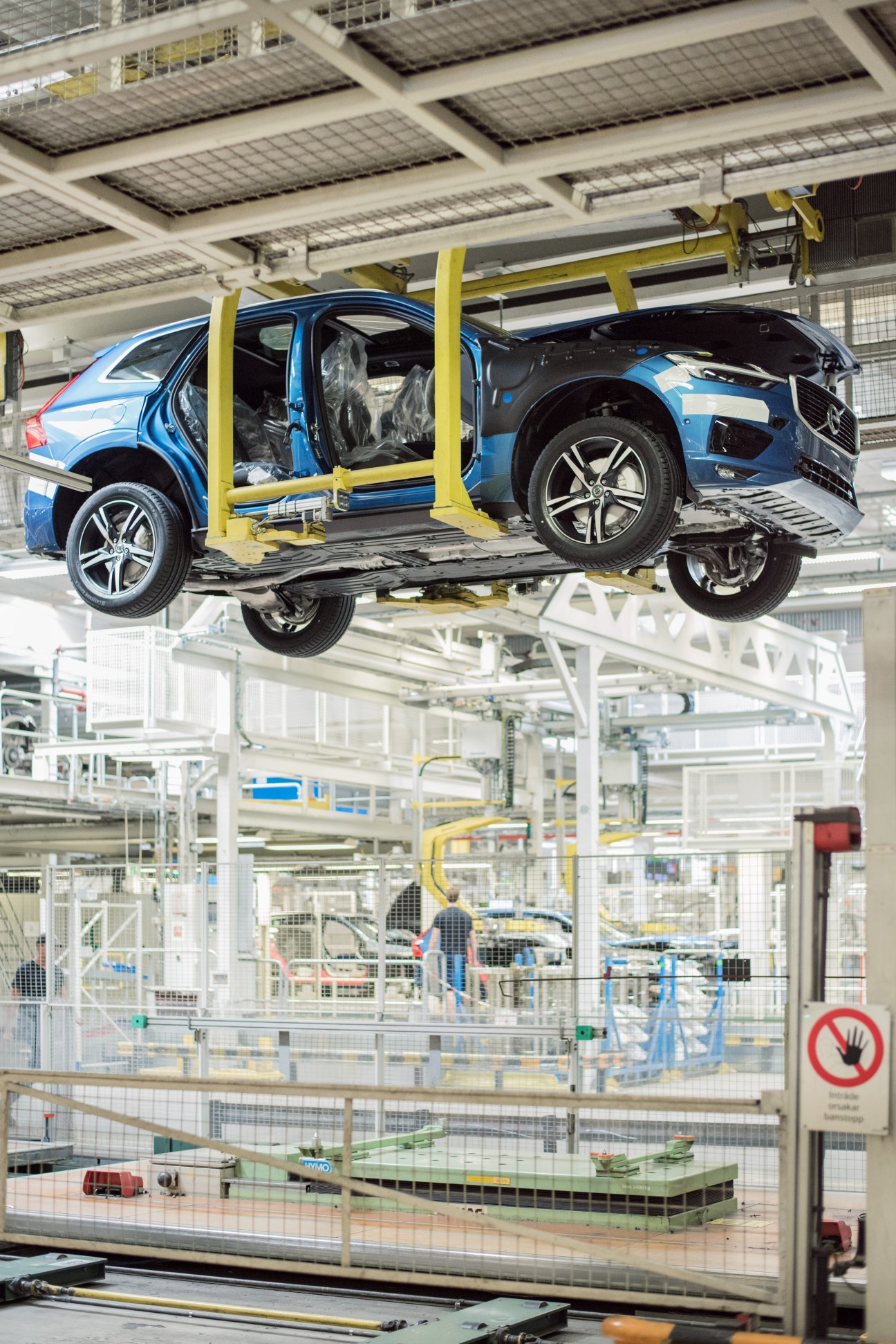 Blue Volvo SUV suspended on yellow lift mechanism in automotive factory assembly line