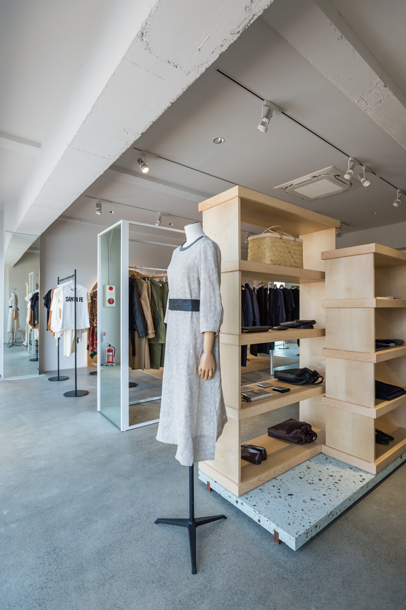 ST Company fashion shop interior with mobile wooden display units and minimal wall shelving showcasing clothing and accessories.