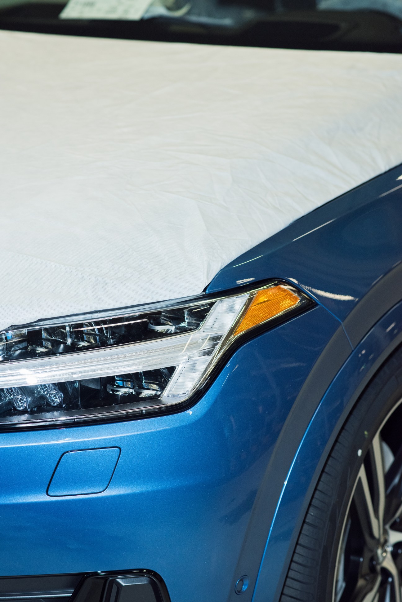 Close-up of blue Volvo car front end showing modern LED headlight and body panel details