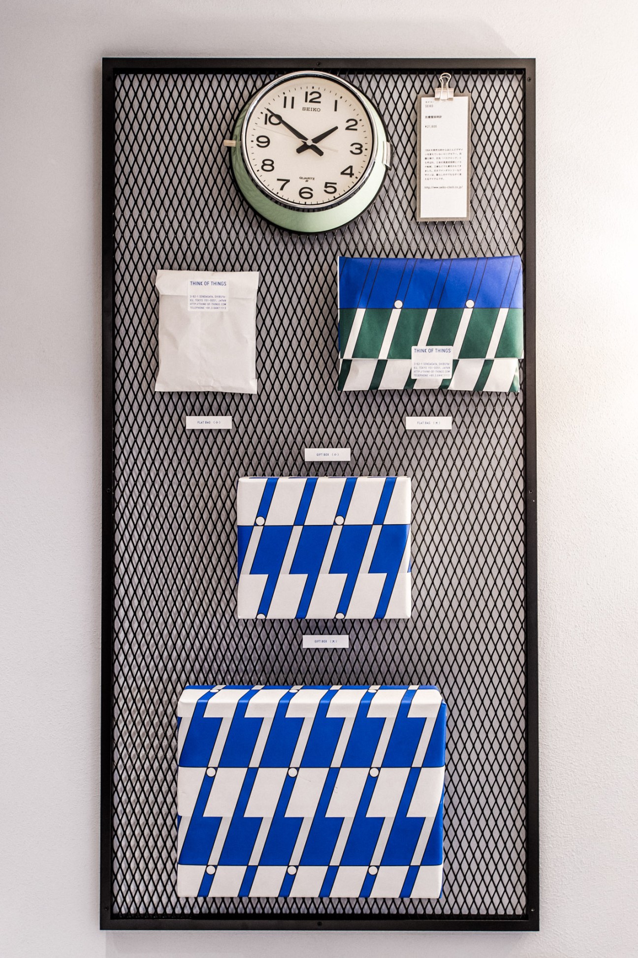 Wall-mounted mesh board displaying colorful notebooks and papers with a round clock