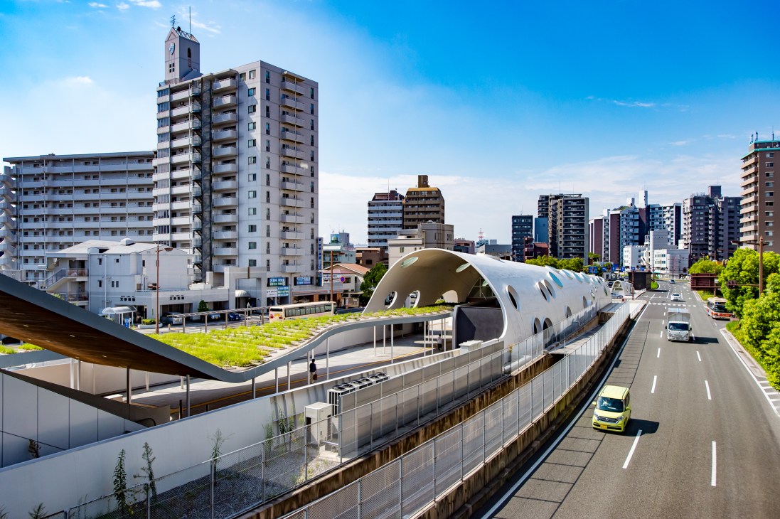 Shinhakushima Station with modern white architecture overlooking Hiroshima cityscape and highway.