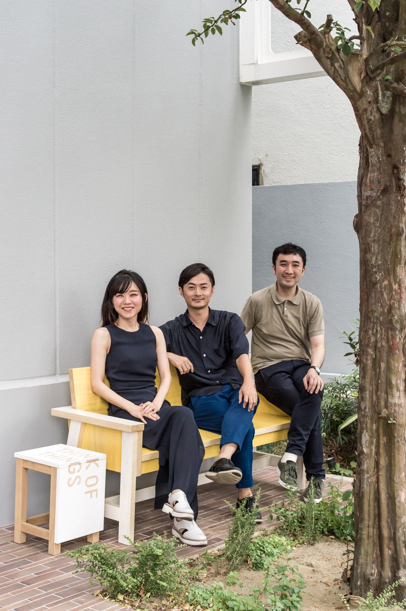 Three Creative Centre members Aki Kanai, Hisashi Kano and Go Hoshi sitting on yellow bench in modern courtyard