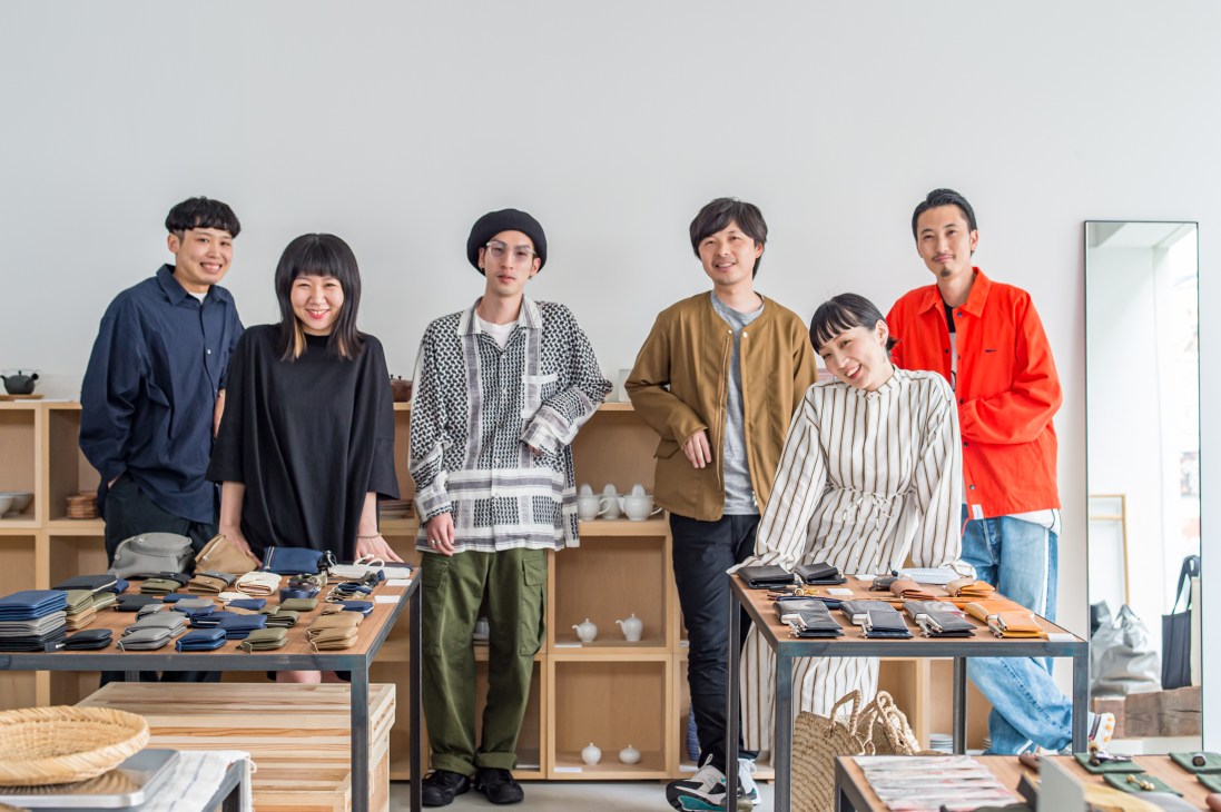 Six smiling staff members standing behind display tables at the lifestyle shop Ref in Hiroshima.