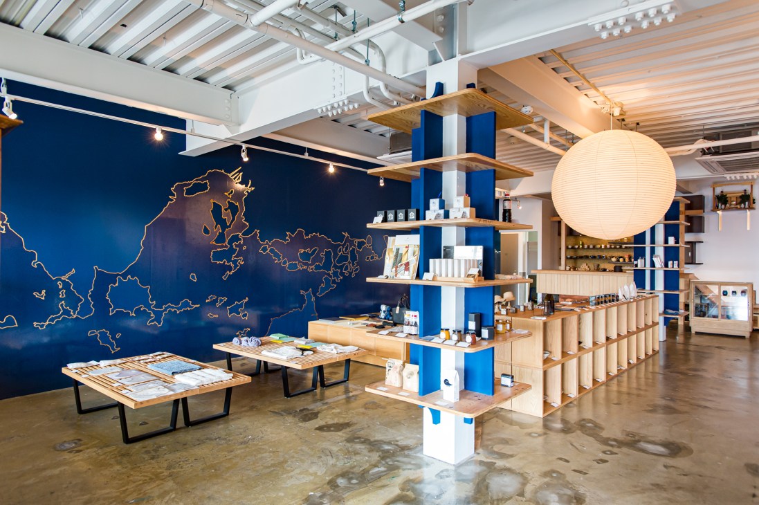 Interior of Engawa shop and restaurant with blue-painted wall featuring gold map outline, wooden shelving, and display tables.