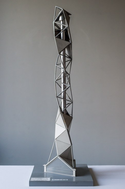 Tall vertical titanium tower mock-up with geometric triangular panels in black and silver tones on a grey base.