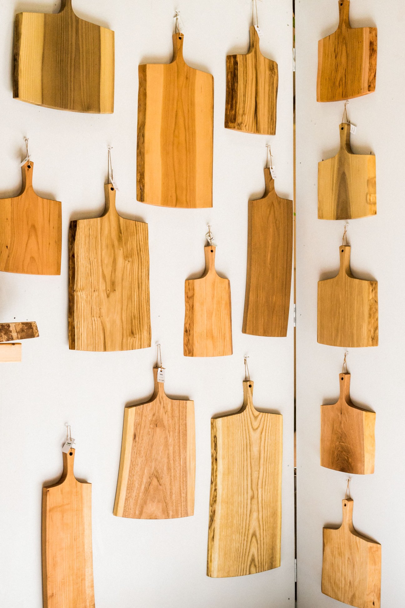 Wooden cutting boards and serving boards of various sizes hanging on a white wall.