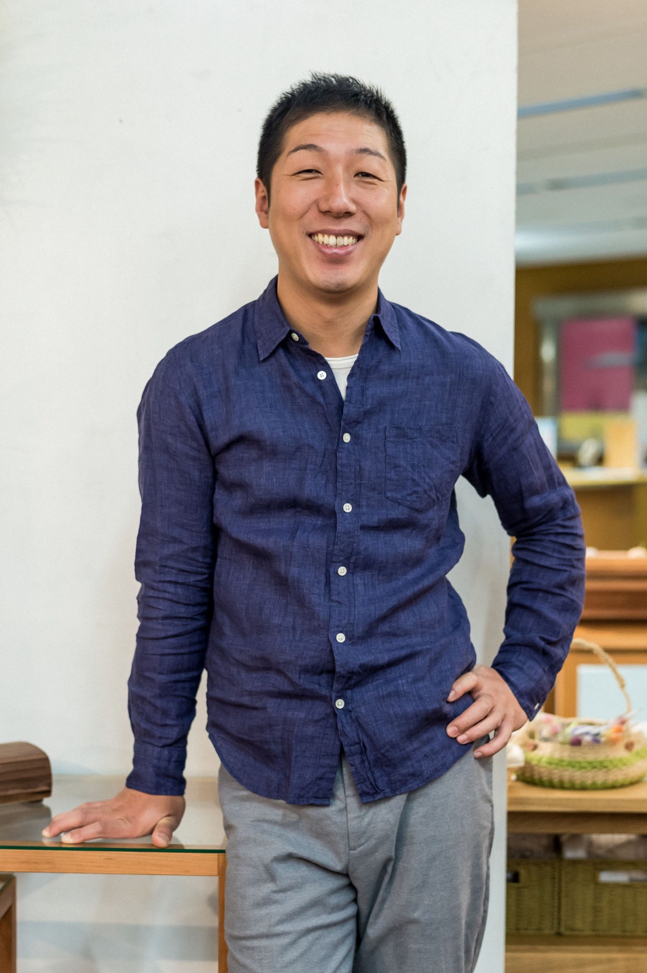 Designer Keita Watanabe smiling in a navy denim shirt in a bright studio setting.