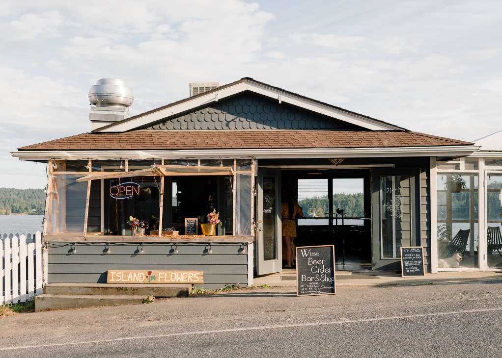 Small wooden building with white picket fence featuring Island Flowers sign and Wine Beer Cider Bar Shop chalkboard