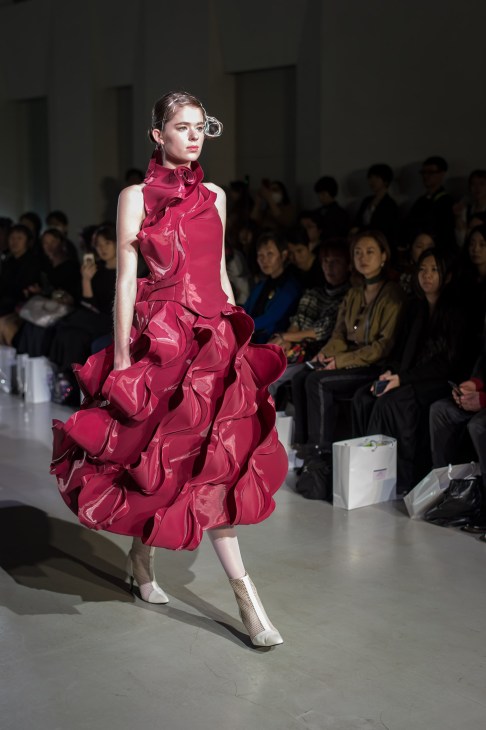 Model wearing a voluminous magenta dress with ruffled skirt and metallic accessories on a runway.