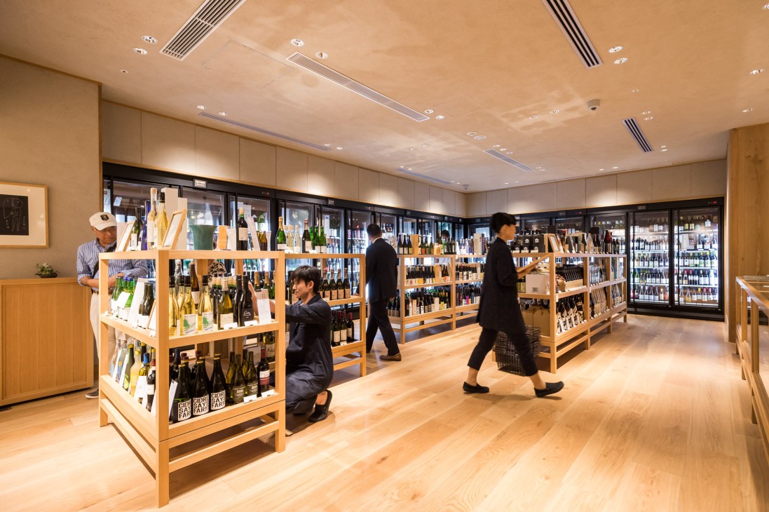 Interior of Imadeya liquor shop with wooden display shelves, refrigerated cases, and customers browsing bottles.