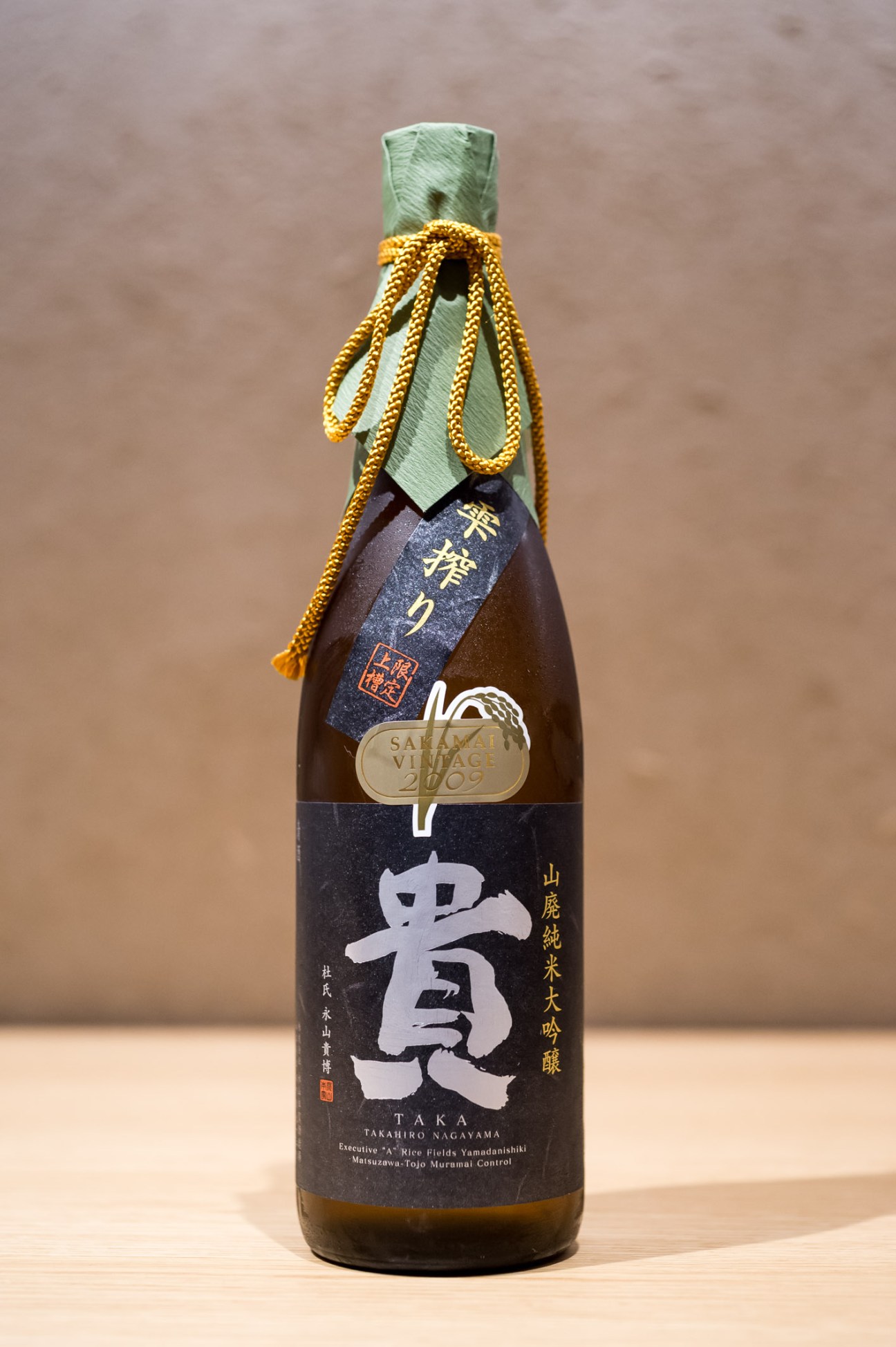 Bottle of Takahiro Nagayama saké with green foil wrapping and gold cord tie.