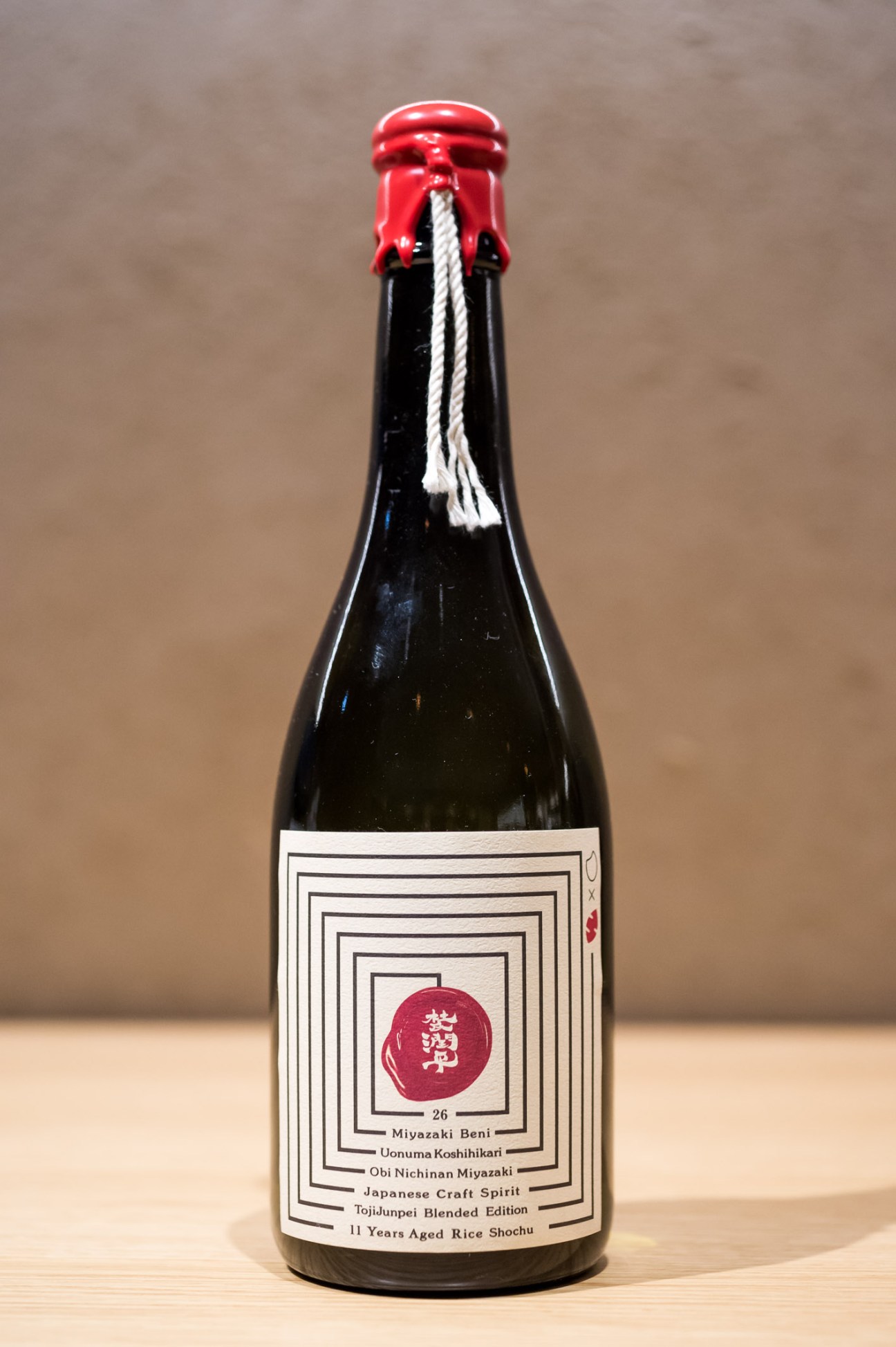 Bottle of Kodama Distillery shochu with red foil seal and white twine against neutral background.