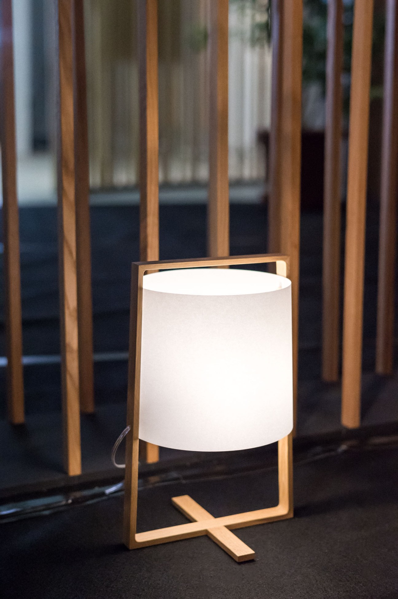H+ standing light in beech by Moare with illuminated cylindrical shade and wooden frame.