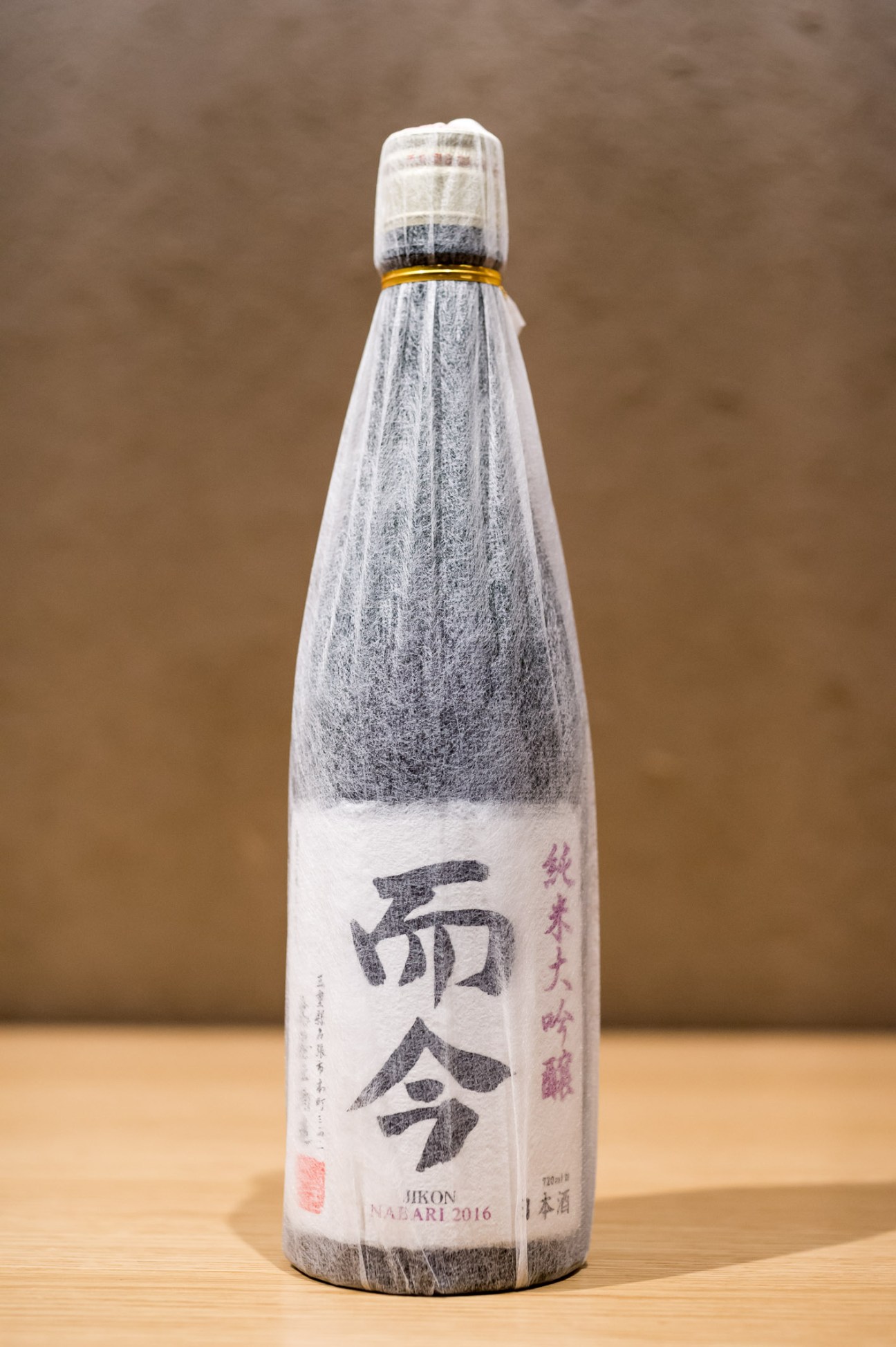 Kiyashou Brewery Jikon saké bottle with white label and gold foil wrapper on wooden surface.