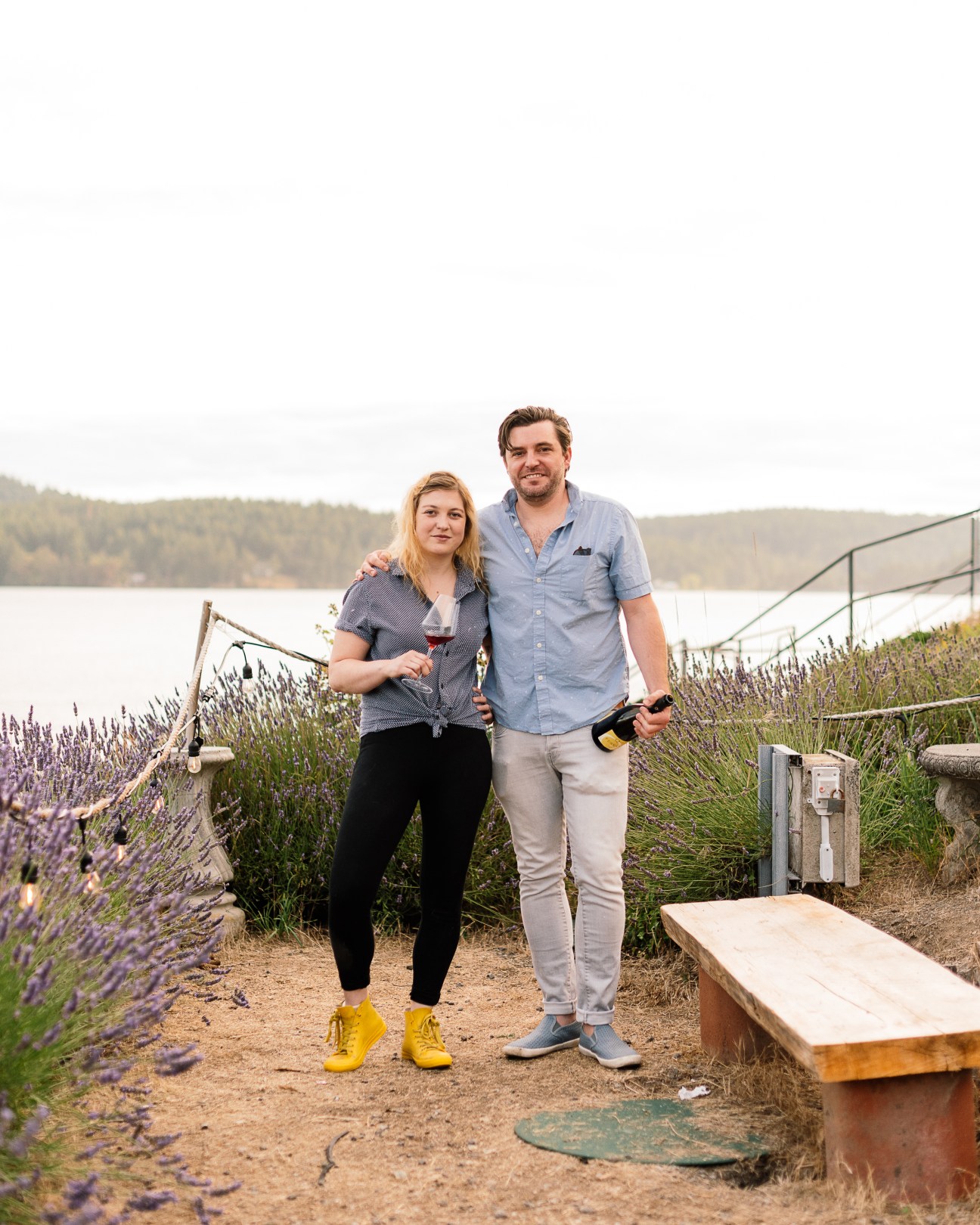 Amelia Carver and Brian Crum standing together outdoors among lavender plants, holding wine bottle and glass