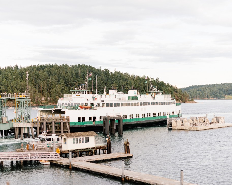Large white and green Washington State ferry docked at Orcas Island terminal with forested hills in background