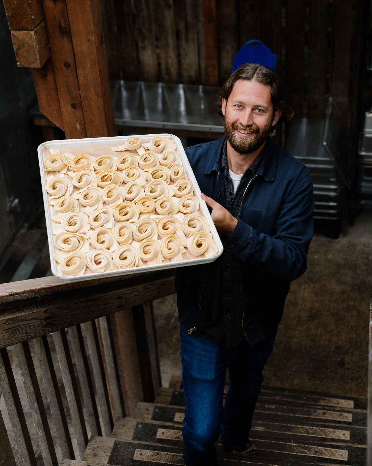 Jon Chappelle holds a tray of handmade pasta spirals in a rustic kitchen setting
