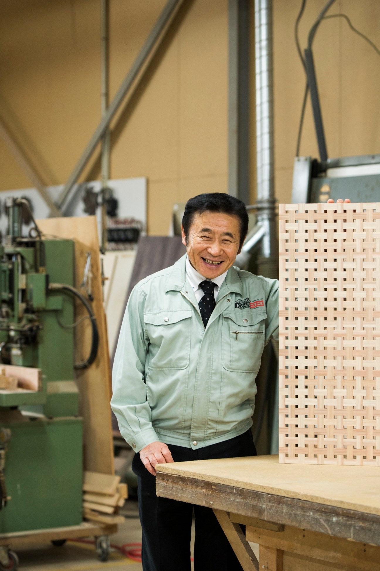 Japanese craftsman in work uniform smiling in woodworking workshop with traditional wooden screens and machinery