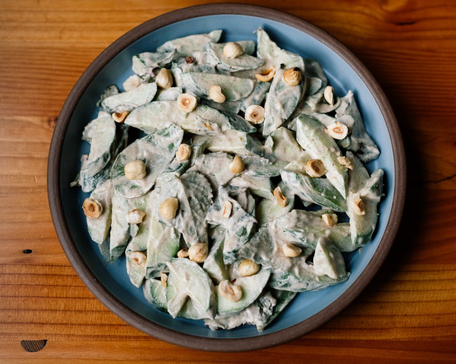 Green vegetable salad with hazelnuts in a blue ceramic bowl on wooden surface