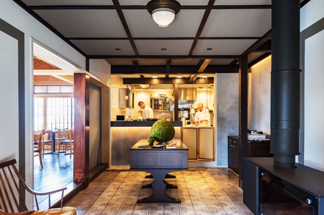 Interior of Lull restaurant with open kitchen, chefs working, and modern minimalist design with dark wooden beams.