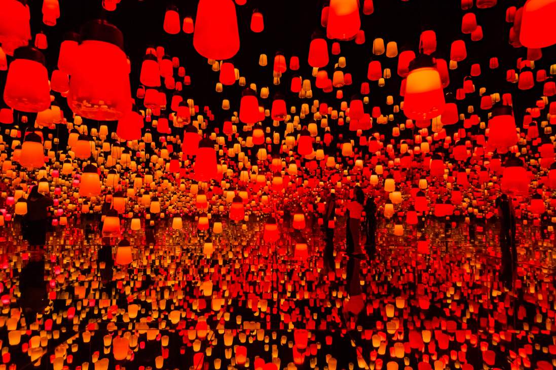 Digital art installation with hundreds of illuminated red and orange lamps suspended in a dark space at TeamLab Borderless.