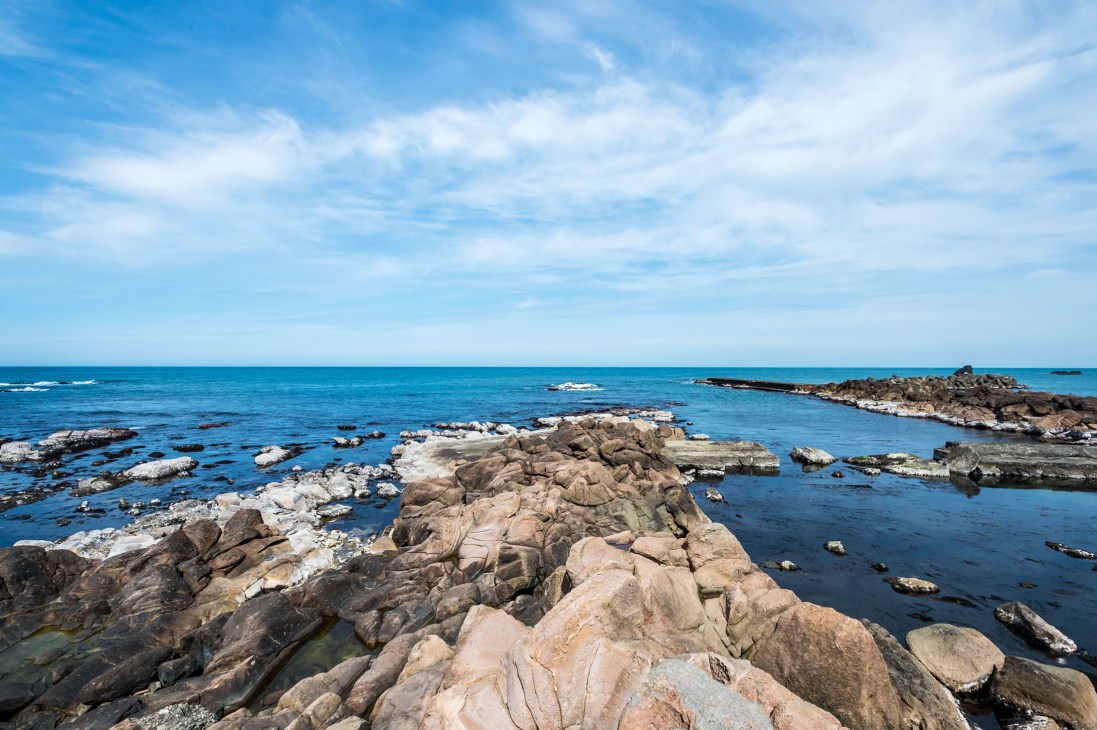 Rocky coastline with boulders extending into blue water under clear sky along the Sea of Japan.