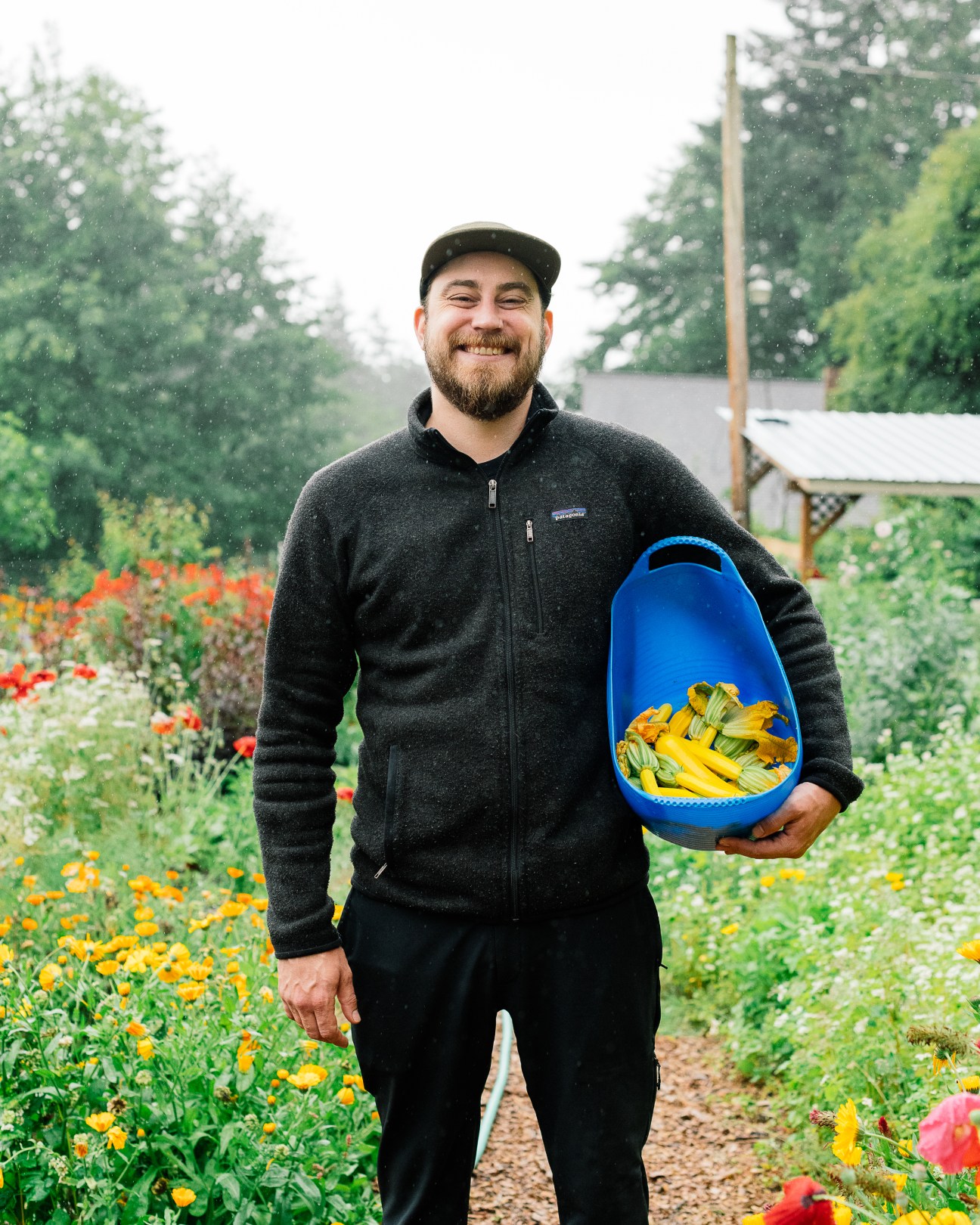 Pete McWilliams, the café's executive chef, smiling while holding a blue basket of yellow squash in a garden