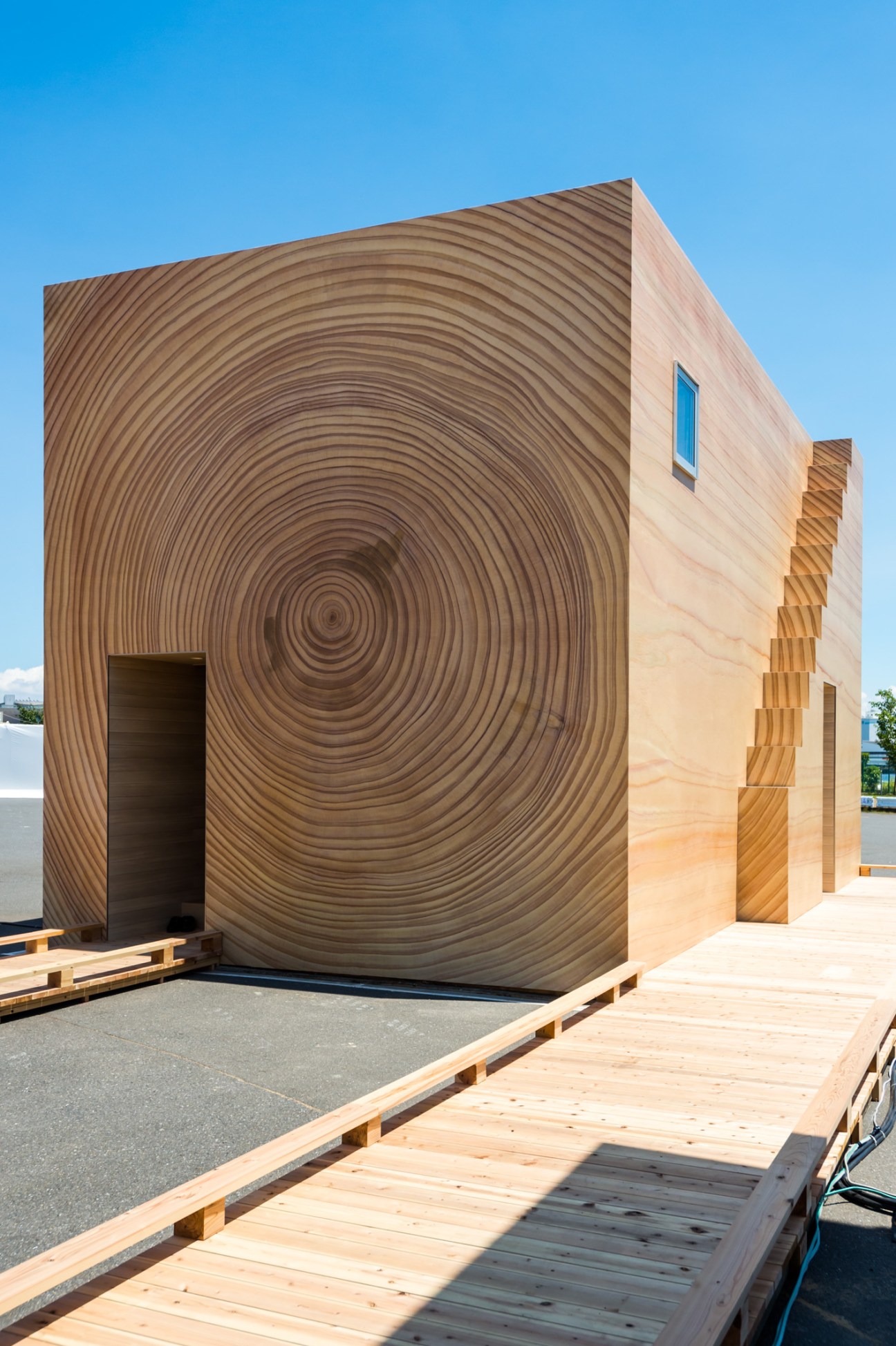 Modern wooden structure with curved concentric circular patterns on facade and blue window detail.