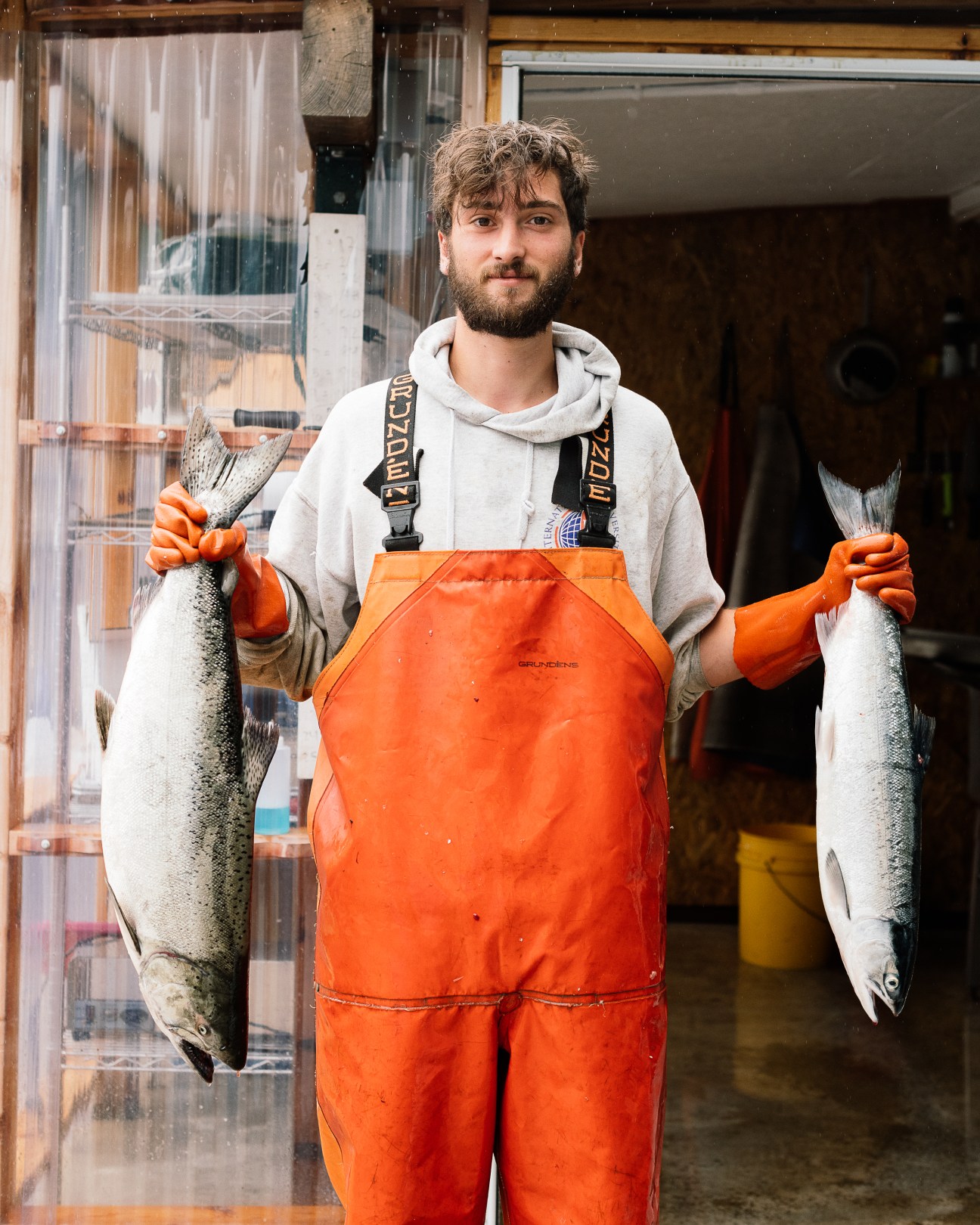 Man in orange waders and gray hoodie holding two large salmon fish at shellfish processing facility