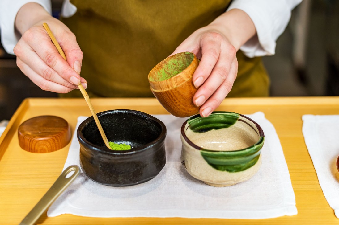 Hands preparing matcha tea with a whisk over two ceramic bowls at Shokudo Yarn.