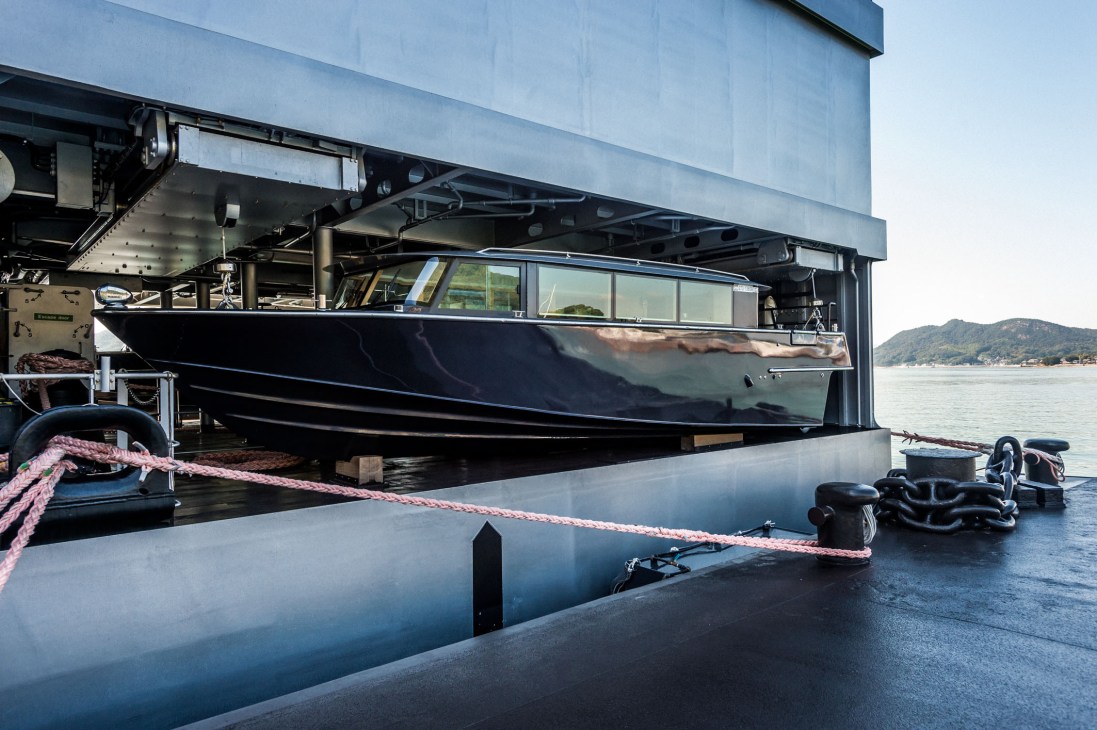 A charcoal-grey motor tender boat designed by architect Yasushi Horibe, secured with pink rope at Guntu's dock.