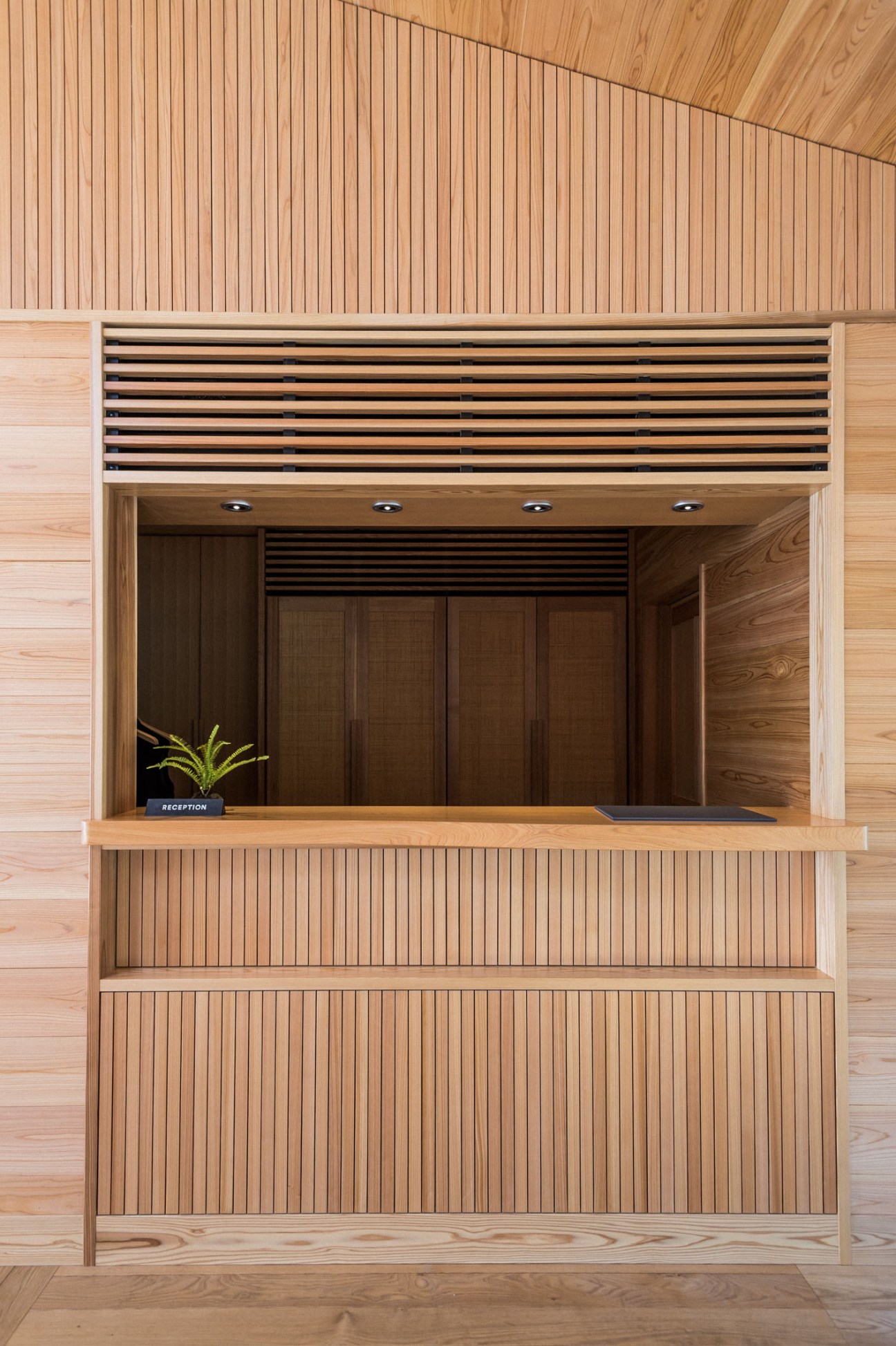 Guntu reception desk with wooden slatted panels and a potted plant on the counter.