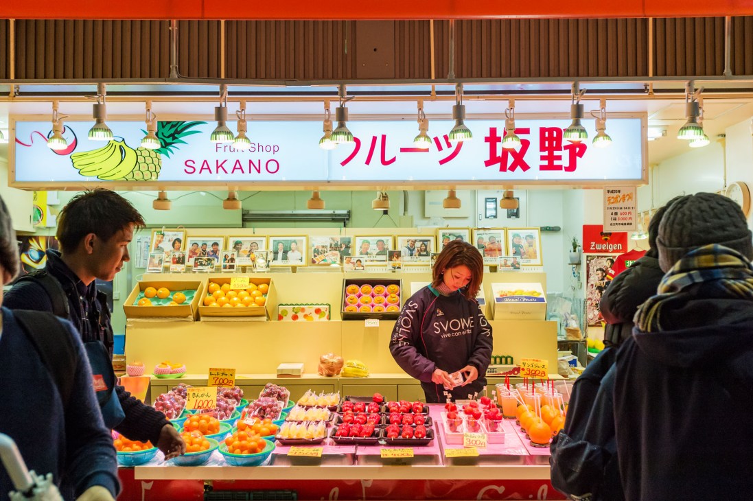 Fruit and vegetable stall at Ohmi-cho market in Japan with vendor and customers.