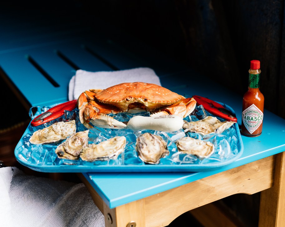 Fresh crab and oysters arranged on ice on a blue tray with Tabasco sauce at Buck Bay Shellfish