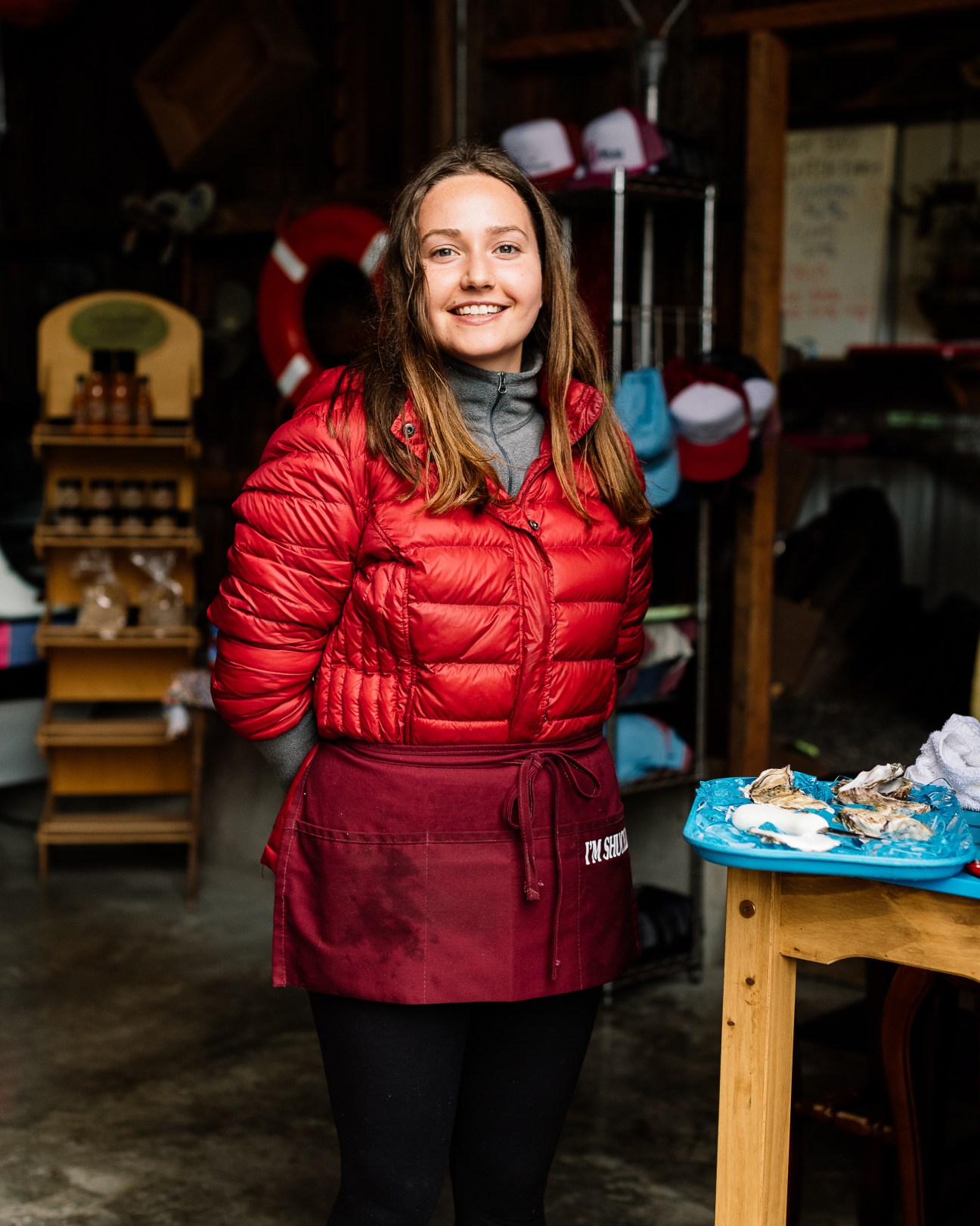 Laura Bergsma from Buck Bay Shellfish Farm wearing red jacket and apron in rustic shellfish processing facility