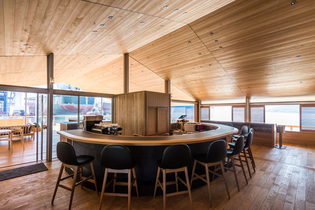 Interior of Guntu's coffee and cocktail bar with wooden ceiling, curved counter, and ocean views through windows.