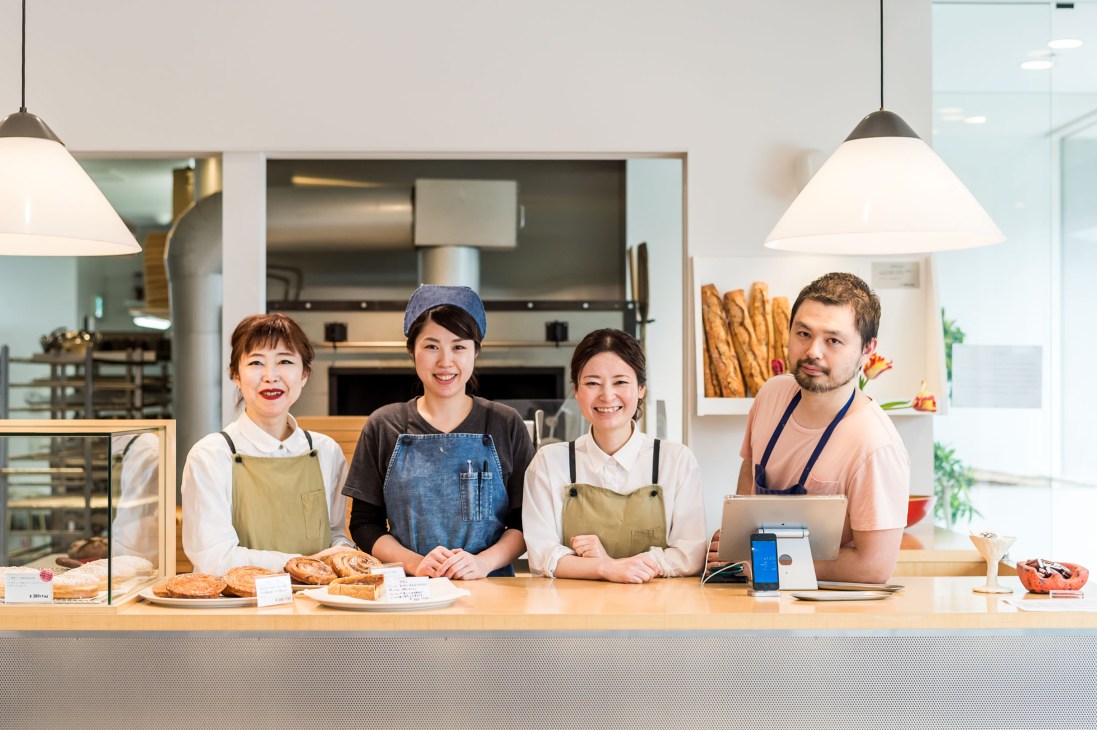 Junji Nio and three team members stand behind the counter at Nior bakery with fresh bread and pastries on display.
