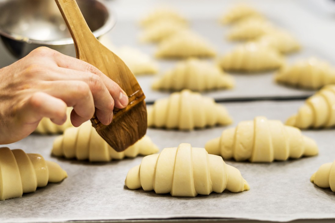 Baker brushing egg wash onto croissant dough with a pastry brush at Nior bakery.