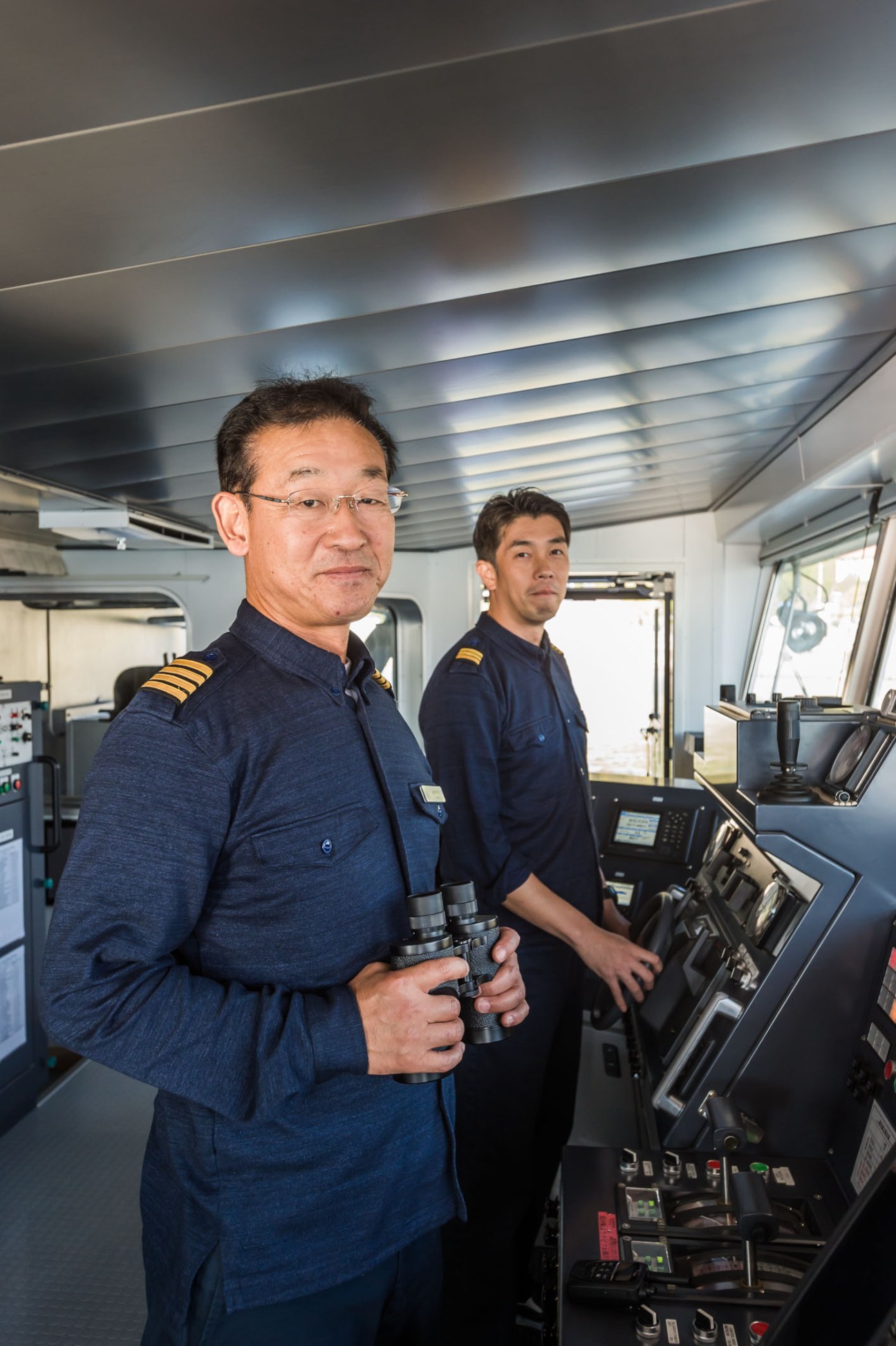 Captain Hirofumi Ochi and chief mate Goro Nishina stand in the ship's bridge wearing navy uniforms.