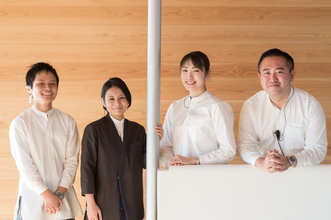 Four Guntu staff members in white and dark uniforms standing in front of a wooden wall.