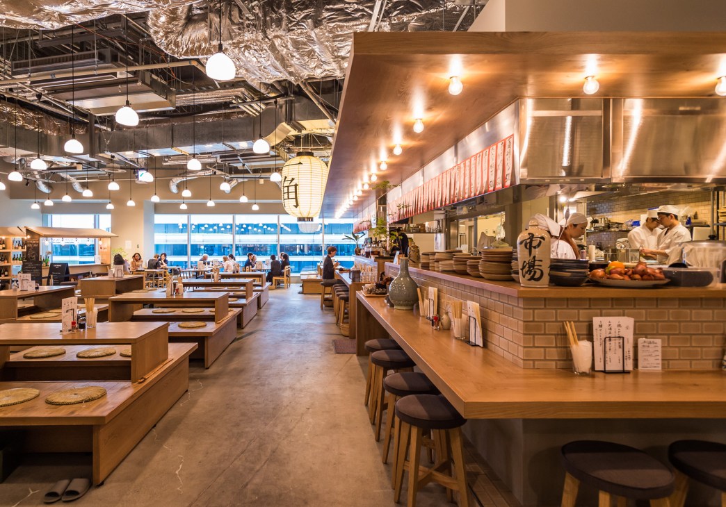 Interior of Ikkaku izakaya restaurant with wooden counters, pendant lighting, and open kitchen.