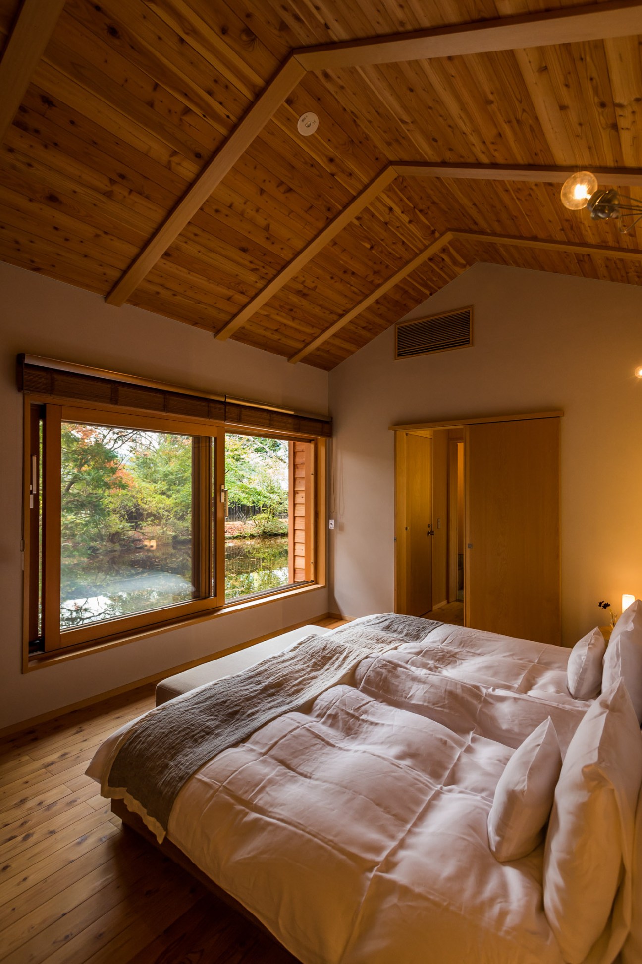 Modern villa bedroom with wooden ceiling, large windows overlooking forest, and natural daylight