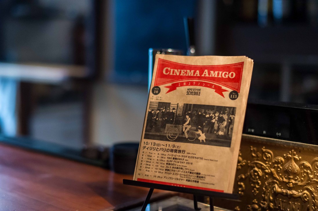 Cinema Amigo program schedule displayed on easel showing movie listings and event details in Japanese