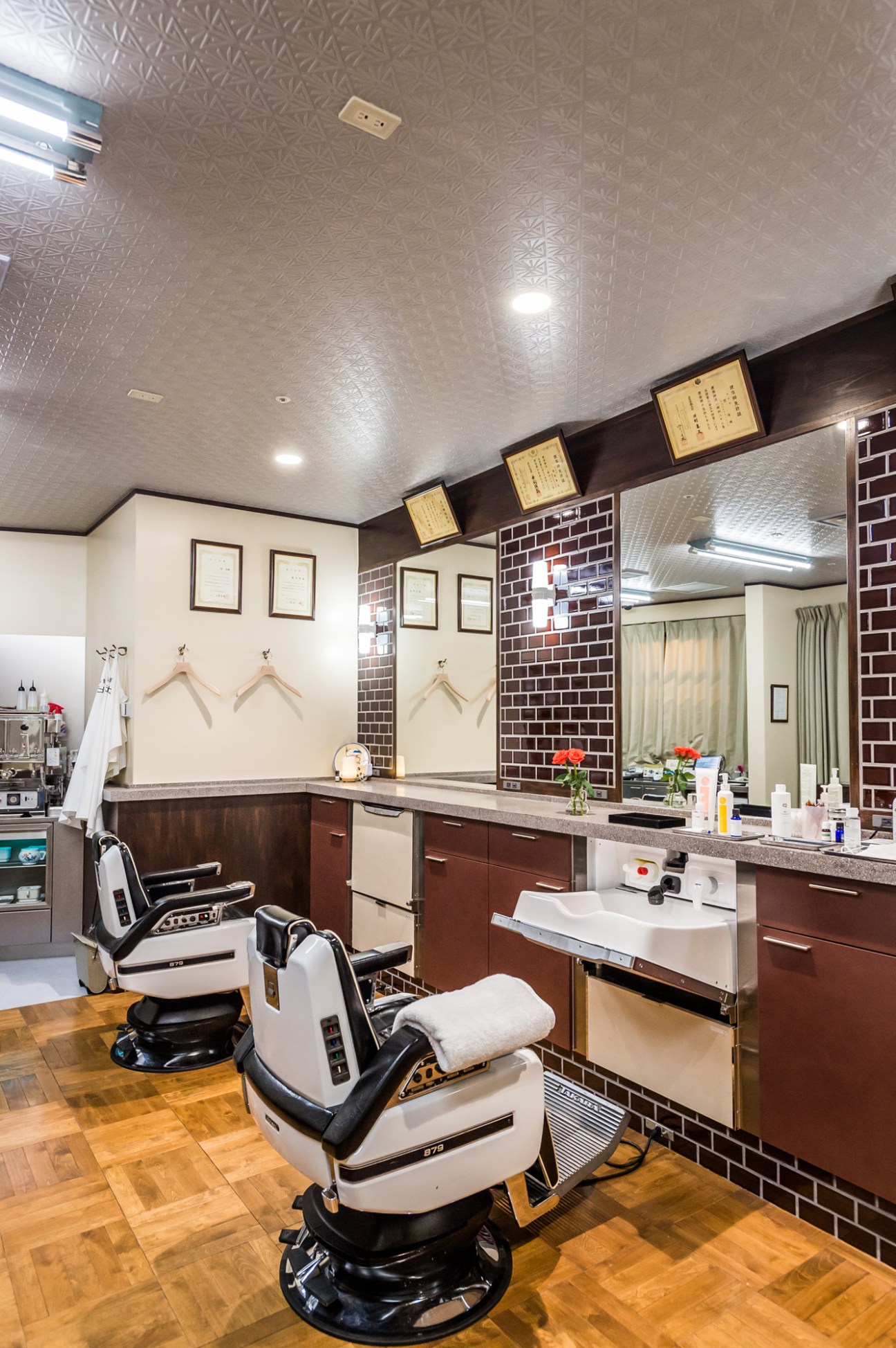 Interior of Barber Hibiya showing vintage barber chairs and red brick walls with framed certificates.